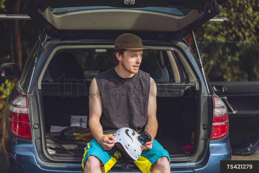 Man with helmet sitting in boot of car