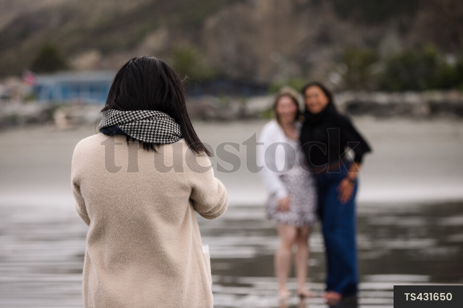 Happy friends smiling on wet beach by coastline