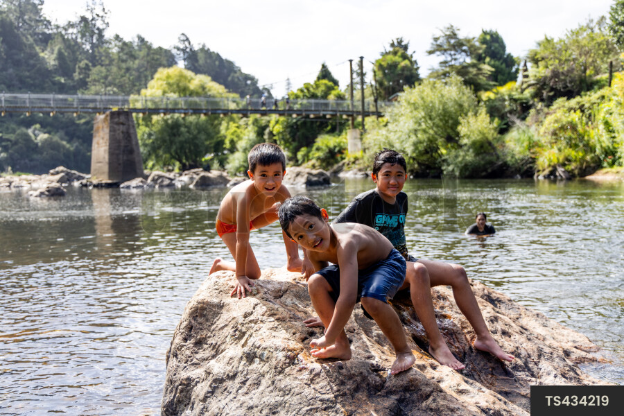 Boys playing on rock by river