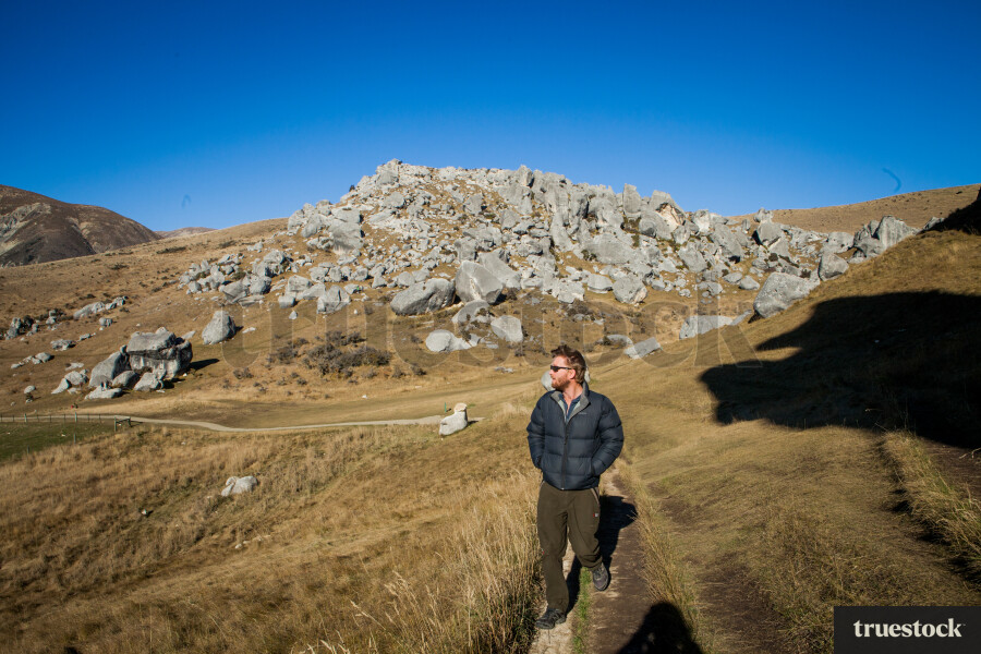 Male adult walking through mountain track and ancient rocks on a clear day