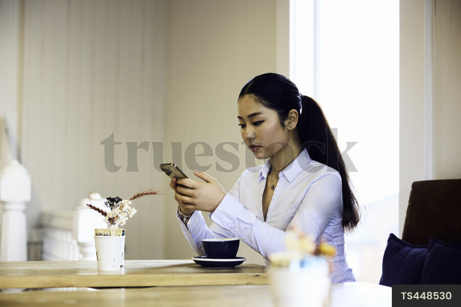 Woman working remotely with smartphone in cafe