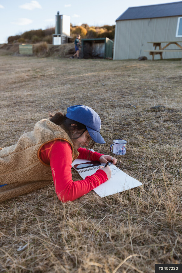 Woman drawing while lying down in field