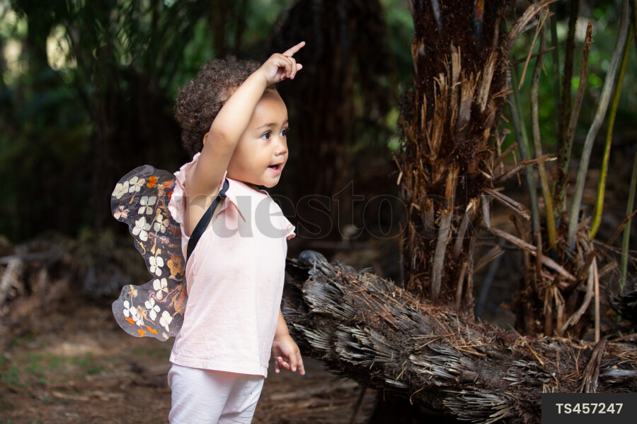 Baby girl wearing fairy wings pointing in garden