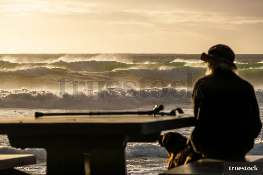 Old man with crutches looking at the beach