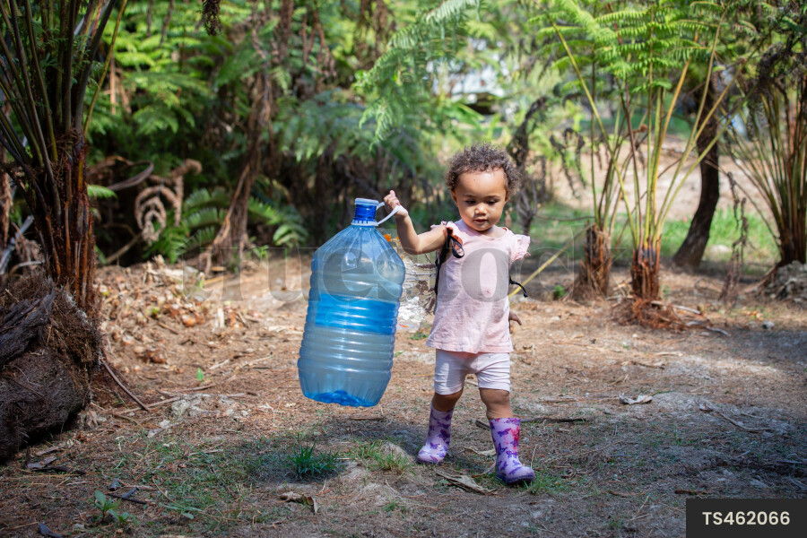 Baby girl carrying bottle while walking through garden
