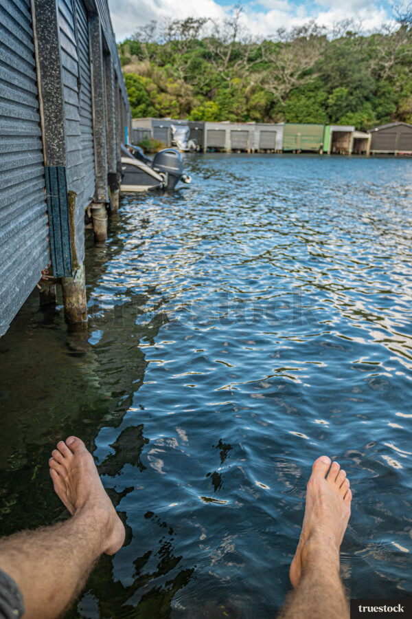 Adult sitting on the edge of the lake with feet dangling above the water