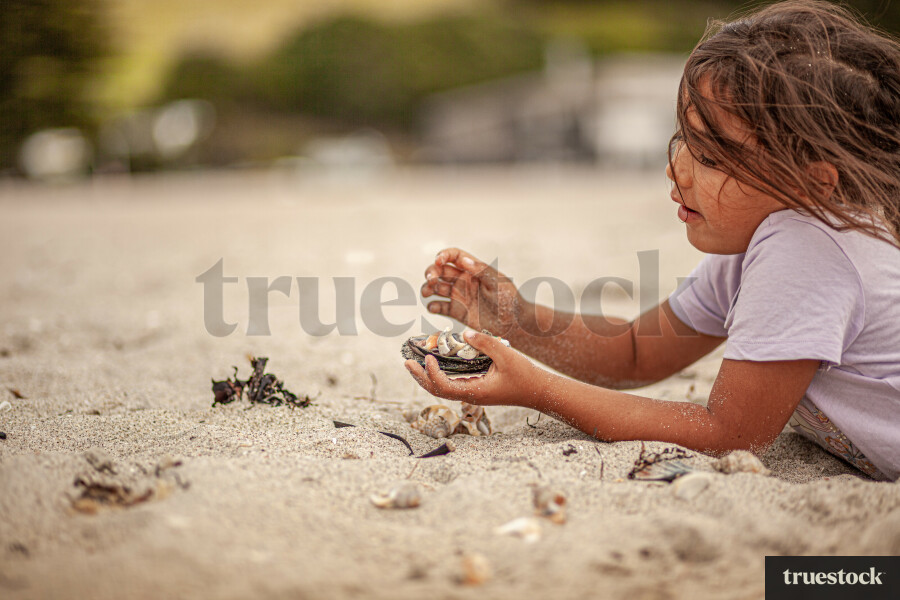 Child lying in the sand collecting shells at the beach