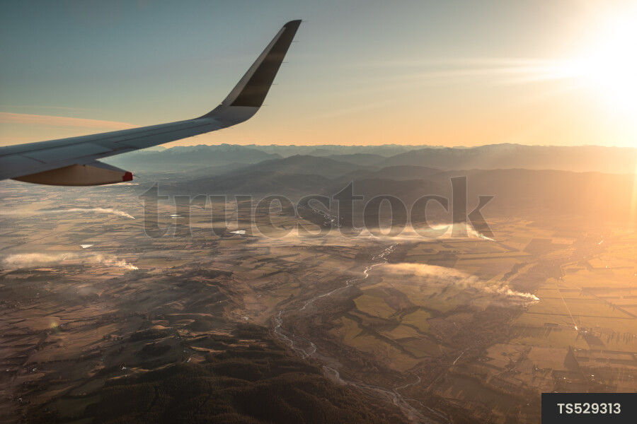 Wing of airplane flying over mountains at sunset