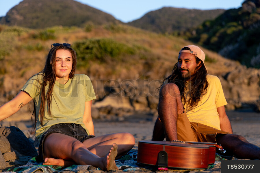 Couple with guitar on beach at sunset