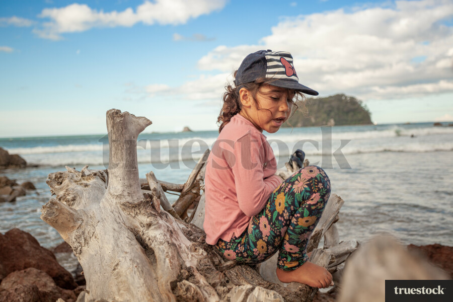 Child sitting on large tree trunk on the beach