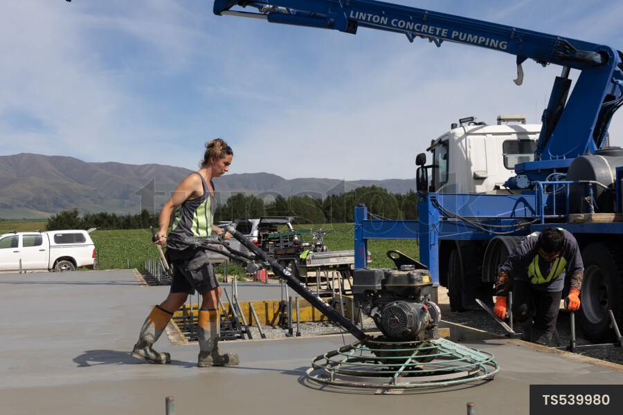Two people working with machine on concrete foundation