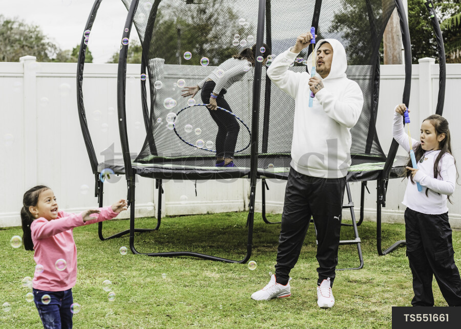 Family playing with bubble wand by trampoline