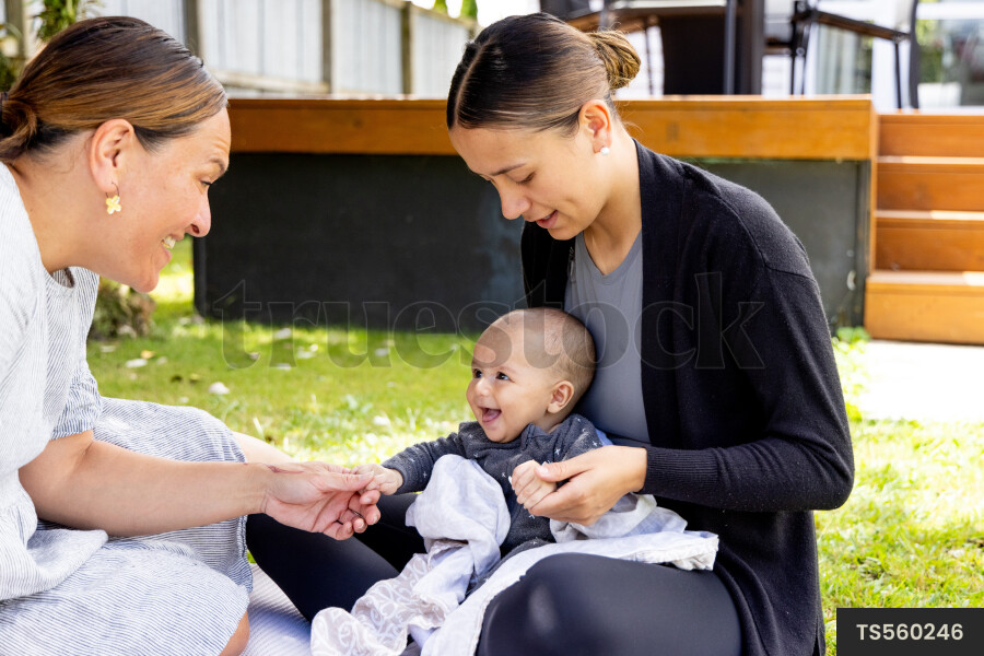 Mother and grandmother with baby boy on picnic blanket
