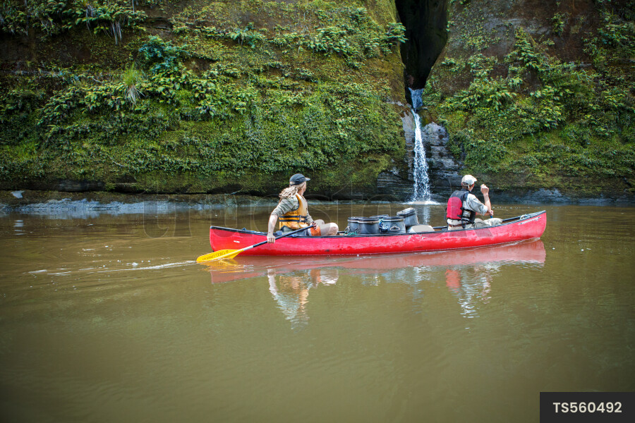 Couple paddling in canoe on river through gorge