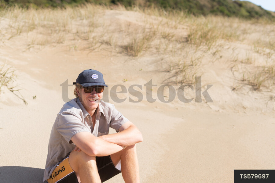 Young man sitting on dunes at beach