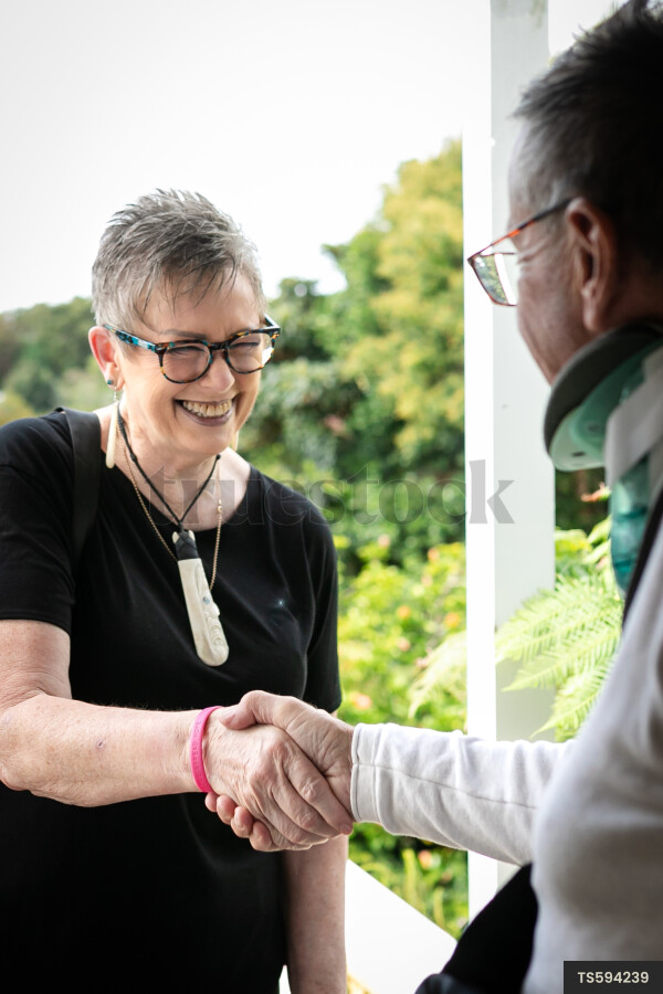 Health carer and patient shaking hands at front door