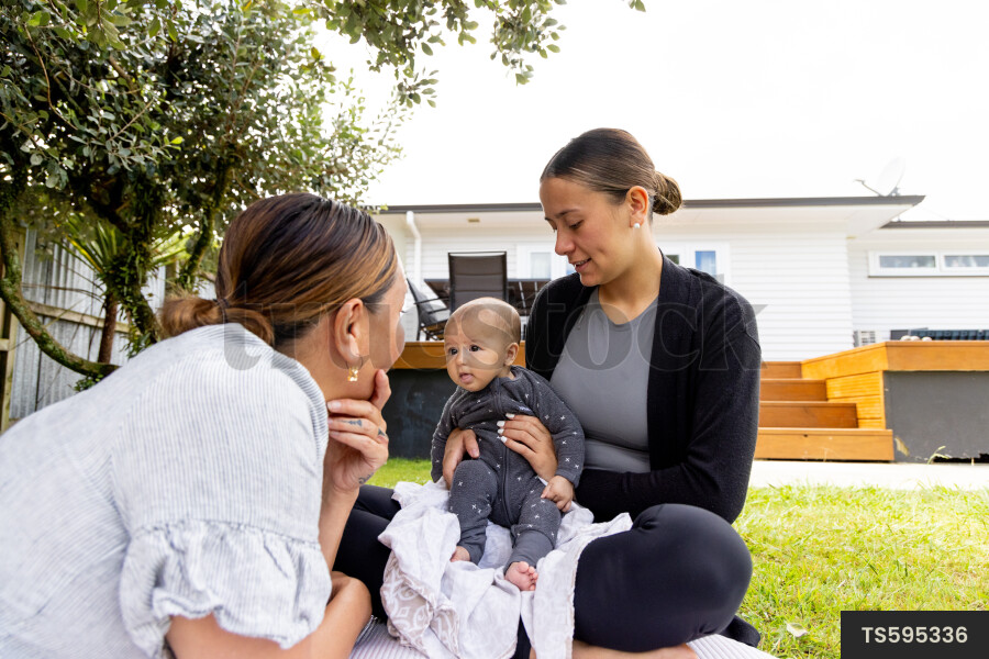 Mother and grandmother with baby boy on picnic blanket