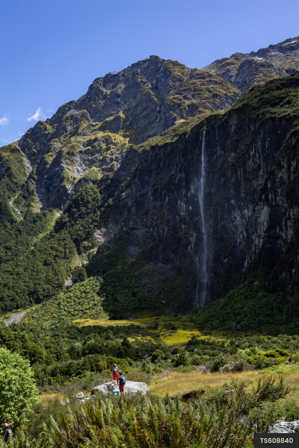 Tourists on rocks next to mountain with waterfall