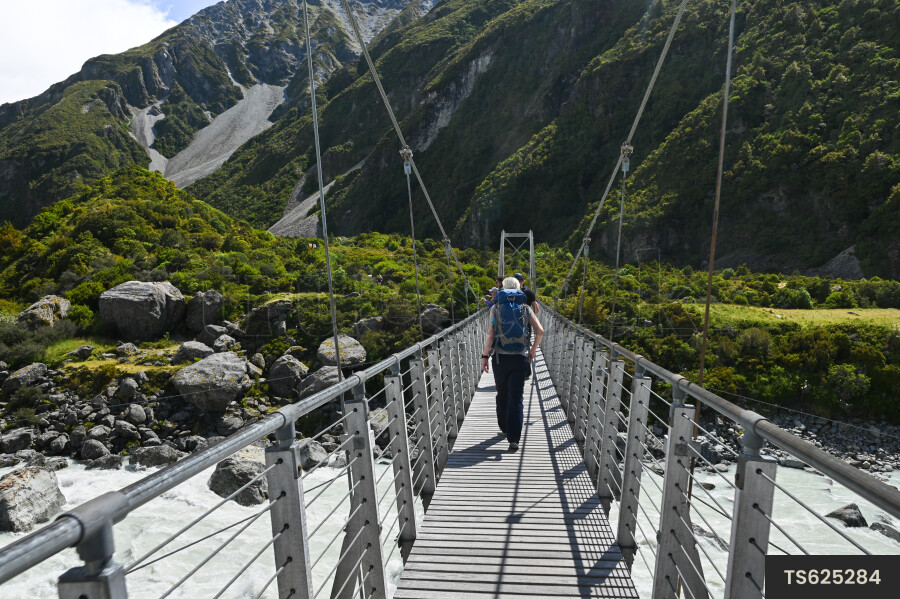 Three people hiking over bridge next to mountain
