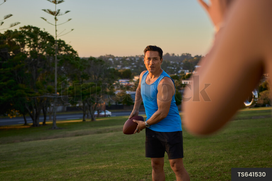 Man throwing rugby ball to woman in park