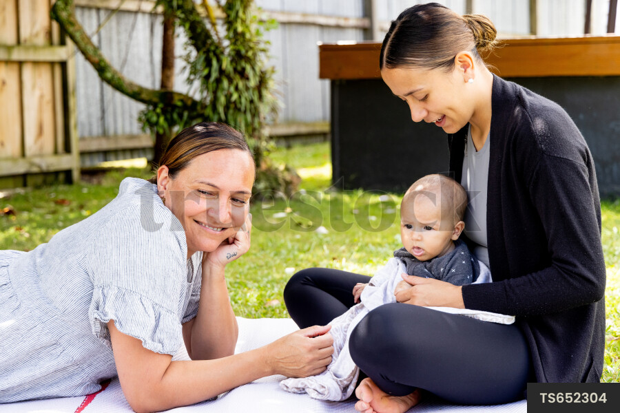Mother and grandmother with baby boy on picnic blanket