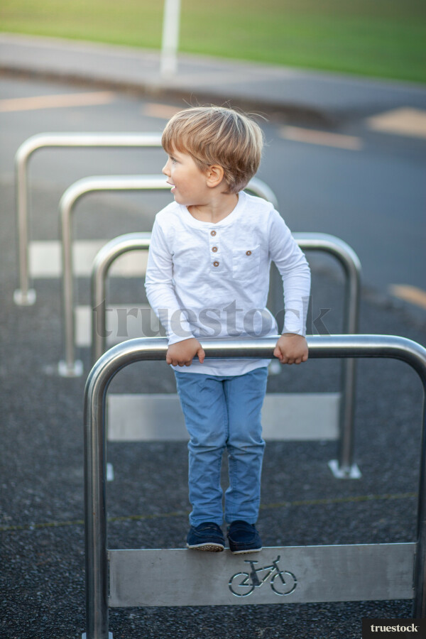 Kid Racking A Bike Child leaning on public bike racks outdoors by Fraser Tebbutt - Truestock