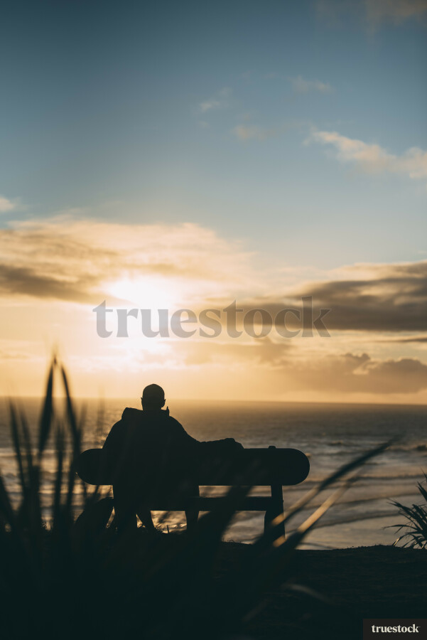 Adult sitting on seat on top of cliff at sunset