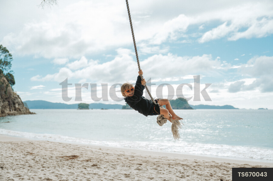 Boy swinging on rope swing at beach
