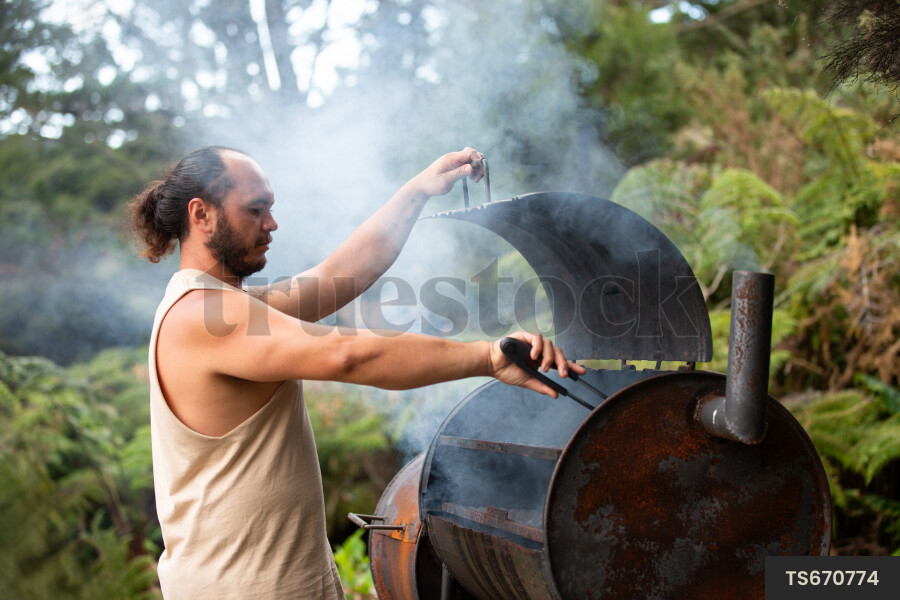 Maori man cooking in barbecue smoker in garden