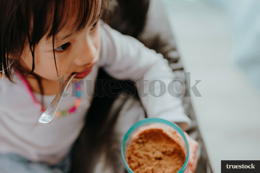 Child eating from ice cream tub on the couch