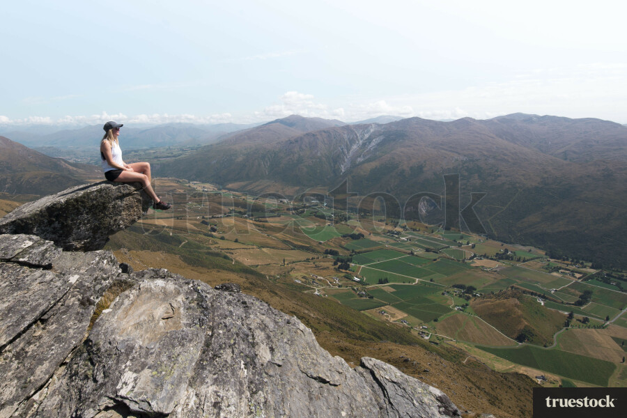 Female adult on cliff rock on top of the mountain looking out below