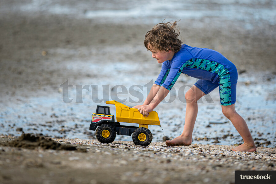 Child playing with toy truck on the sand at the beach