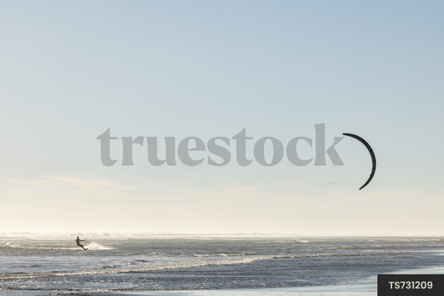 Silhouette of man kitesurfing on waves in sea