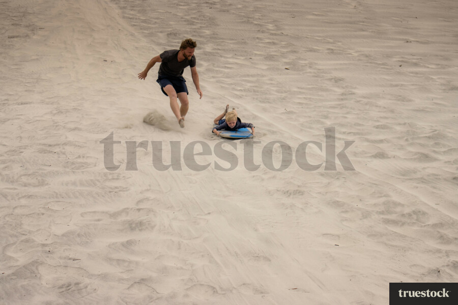 Child sand boarding down sand dunes on a boogie board at the beach