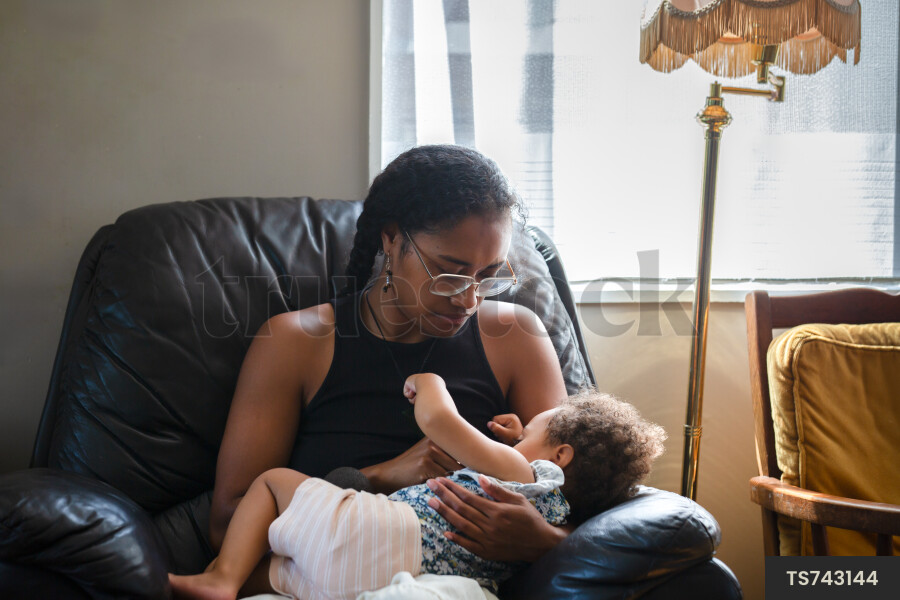 Mother breastfeeding daughter on armchair in house