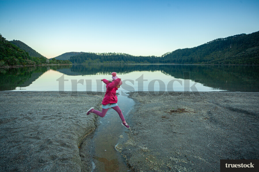 Child running and jumping over water creek by the lake