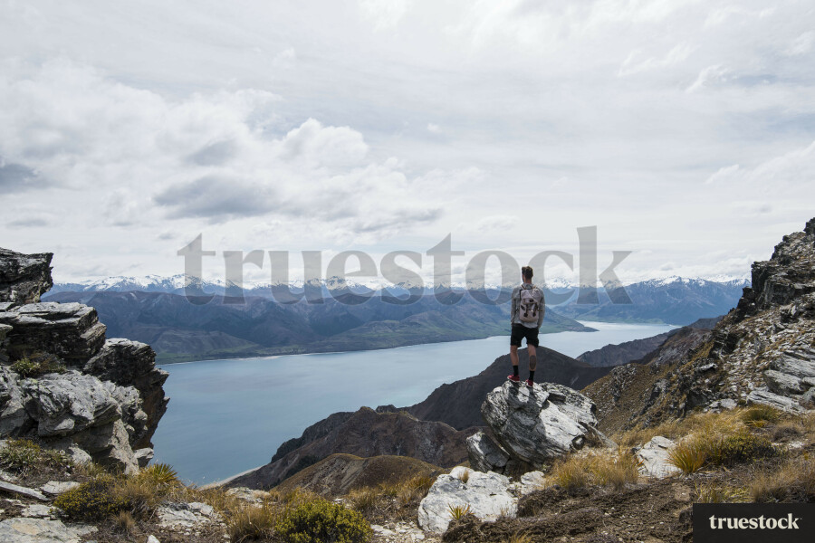 Male adult standing on the edge of the cliff on top of the mountain overlooking the lake