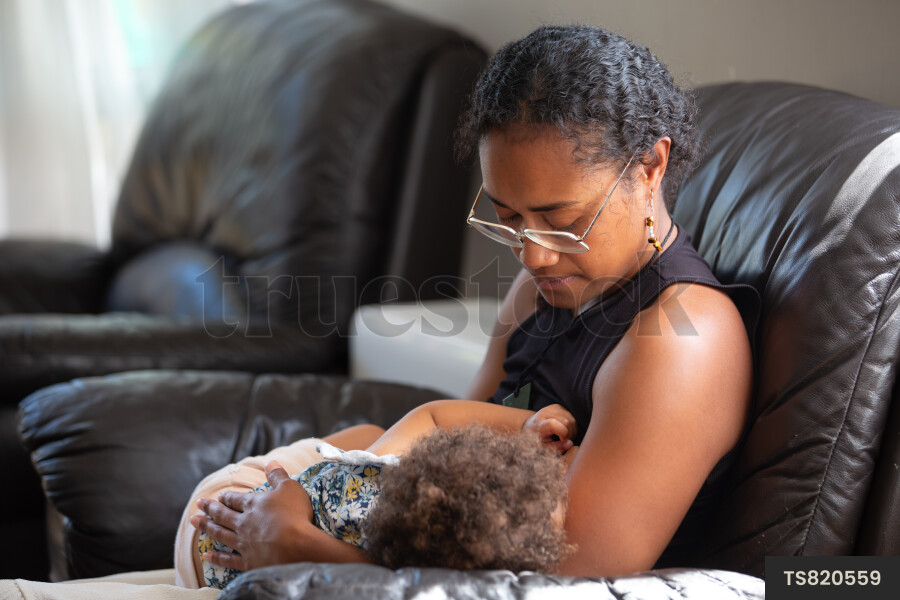Mother breastfeeding daughter on armchair in house