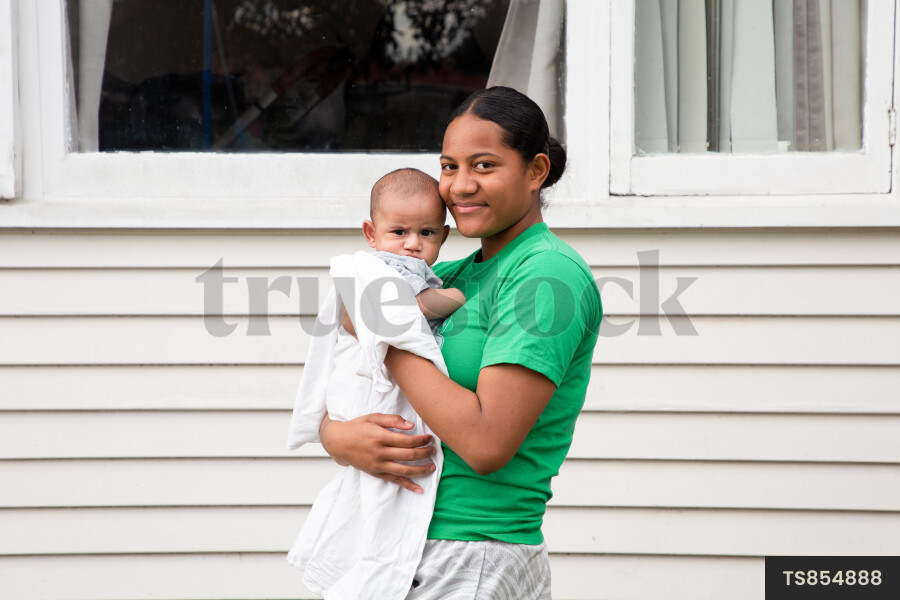 Tongan sister holding baby brother outside house