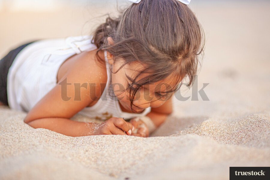 Child lying down in the sand at the beach
