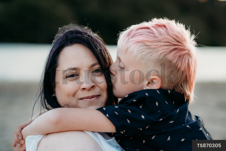 Son kissing mother on cheek by coastline