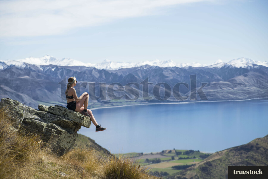 Female adult sitting on mountain cliff rock overlooking the lake