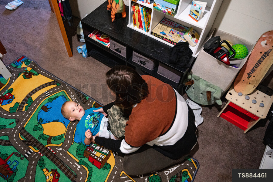 Mother caring for son wearing diaper in bedroom