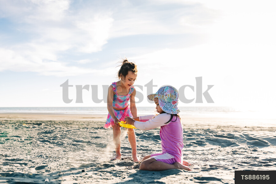 Sisters in swimsuits playing with toy on beach