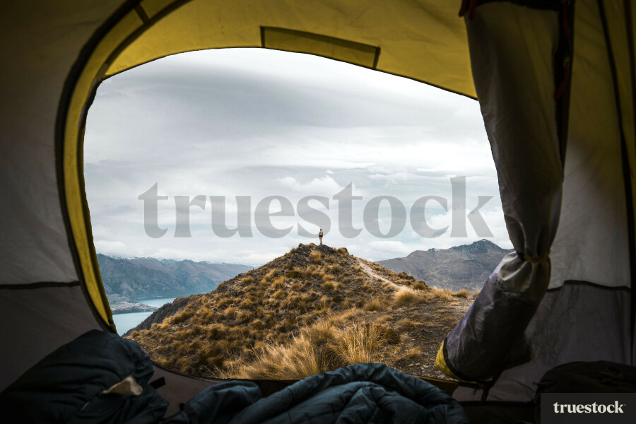 View from inside of a tent on top of mountain with adult standing on a peak