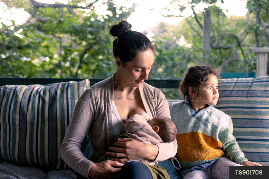 Mother breastfeeding newborn daughter with niece in living room
