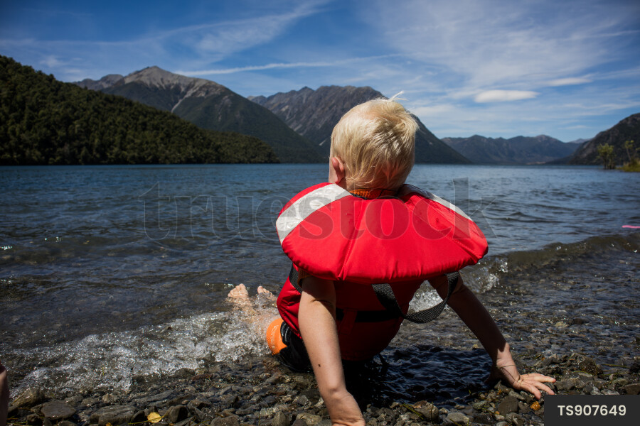 Boy with life jacket sitting by Lake Hurunui