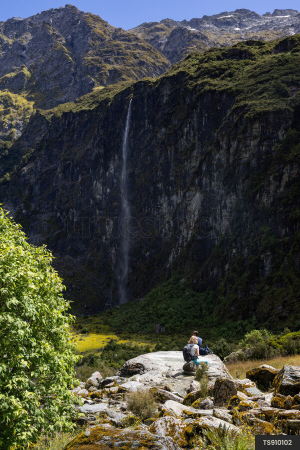 Tourists on rocks next to mountain with waterfall