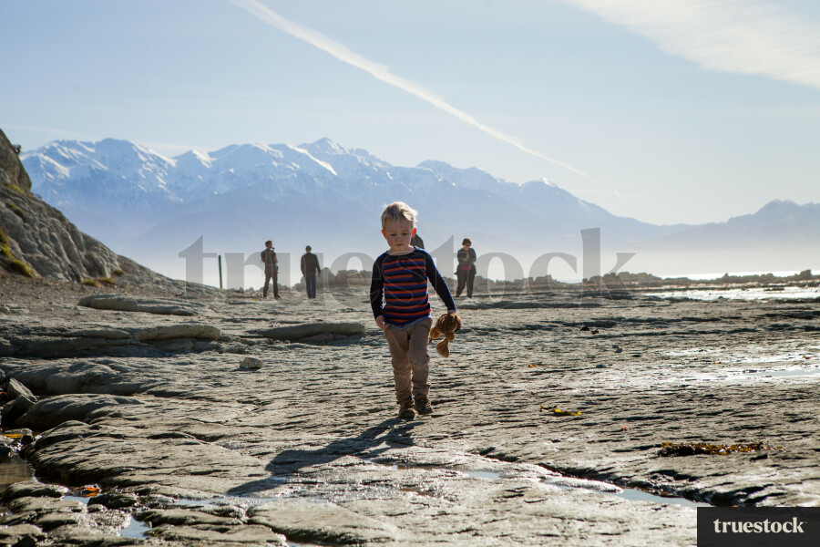 Child walking on the rocks holding a soft toy at the beach