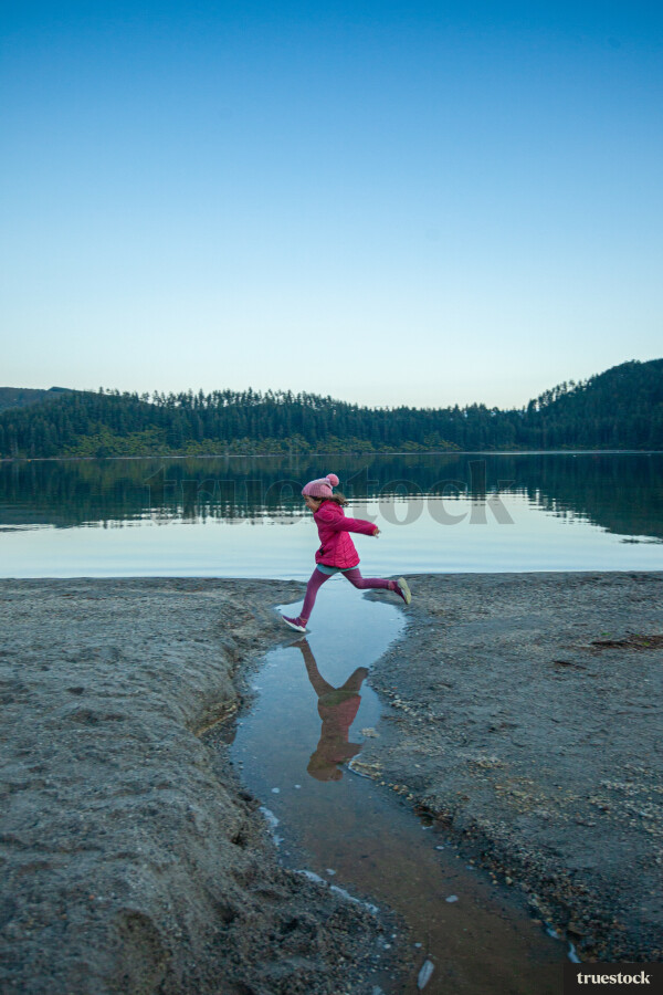 Child running and jumping over water creek by the lake